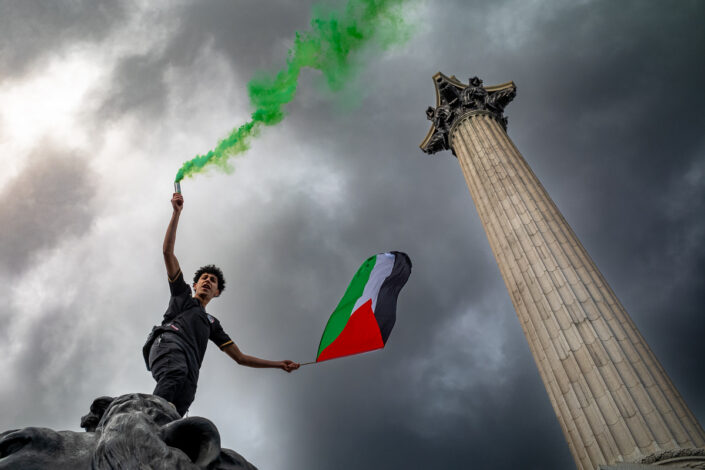 A protester holds a green flare and Palestinian flag in support of Gaza, Trafalgar Square, London, UK