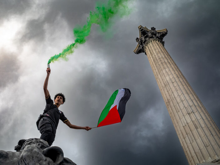 A protester holds a green flare and Palestinian flag in support of Gaza, Trafalgar Square, London, UK