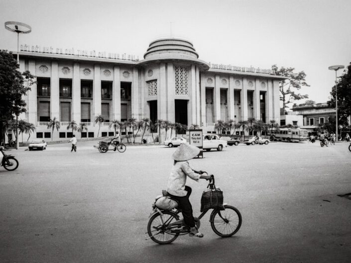 A woman cycles past the State Bank of Vietnam, 1992 / Một người phụ nữ đạp xe ngang qua Ngân hàng Nhà nước Việt Nam, 1992