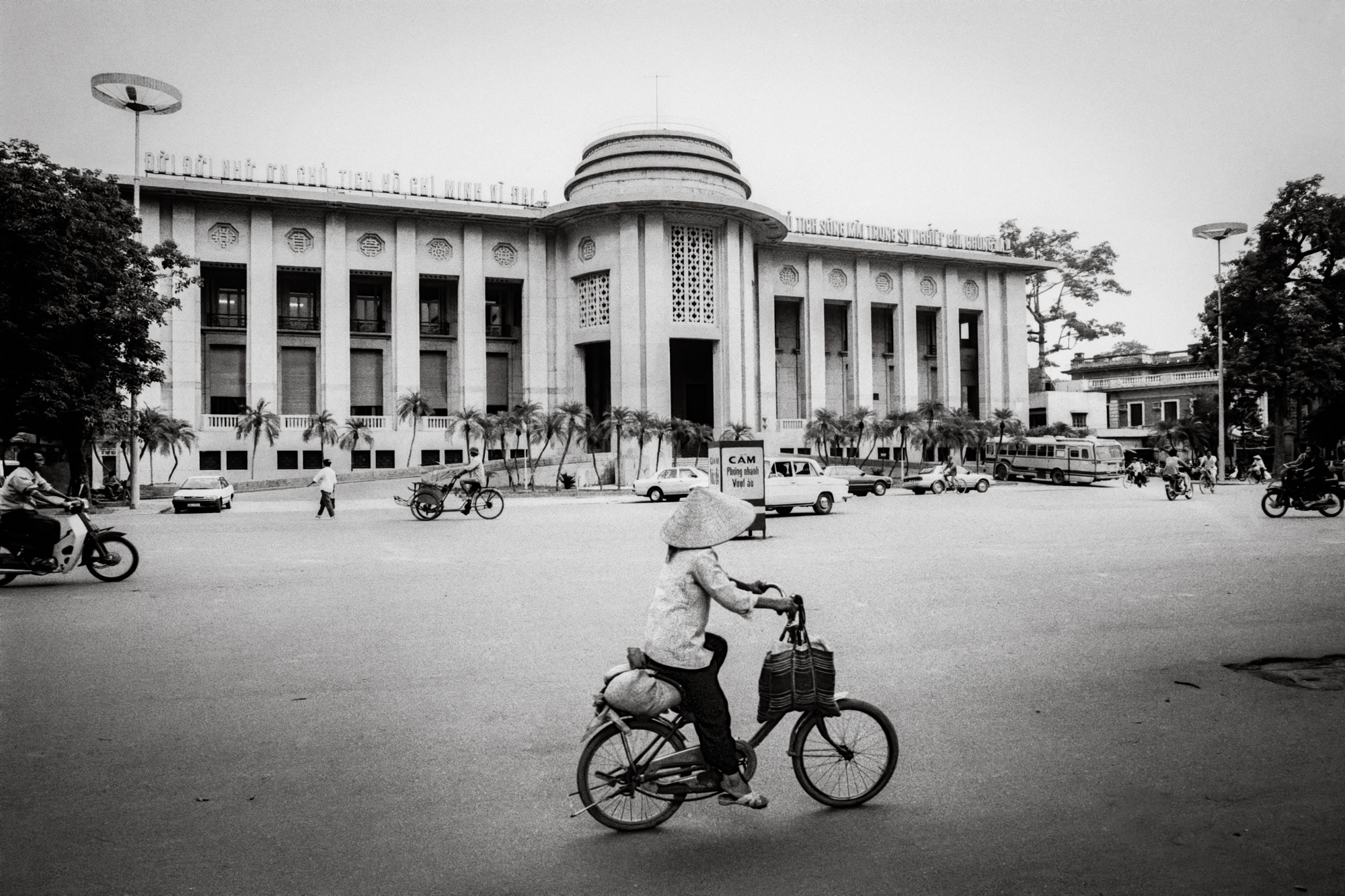 A woman cycles past the State Bank of Vietnam, 1992 / Một người phụ nữ đạp xe ngang qua Ngân hàng Nhà nước Việt Nam, 1992